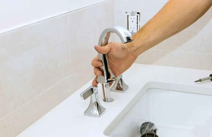 Hand installing a chrome faucet on a sink