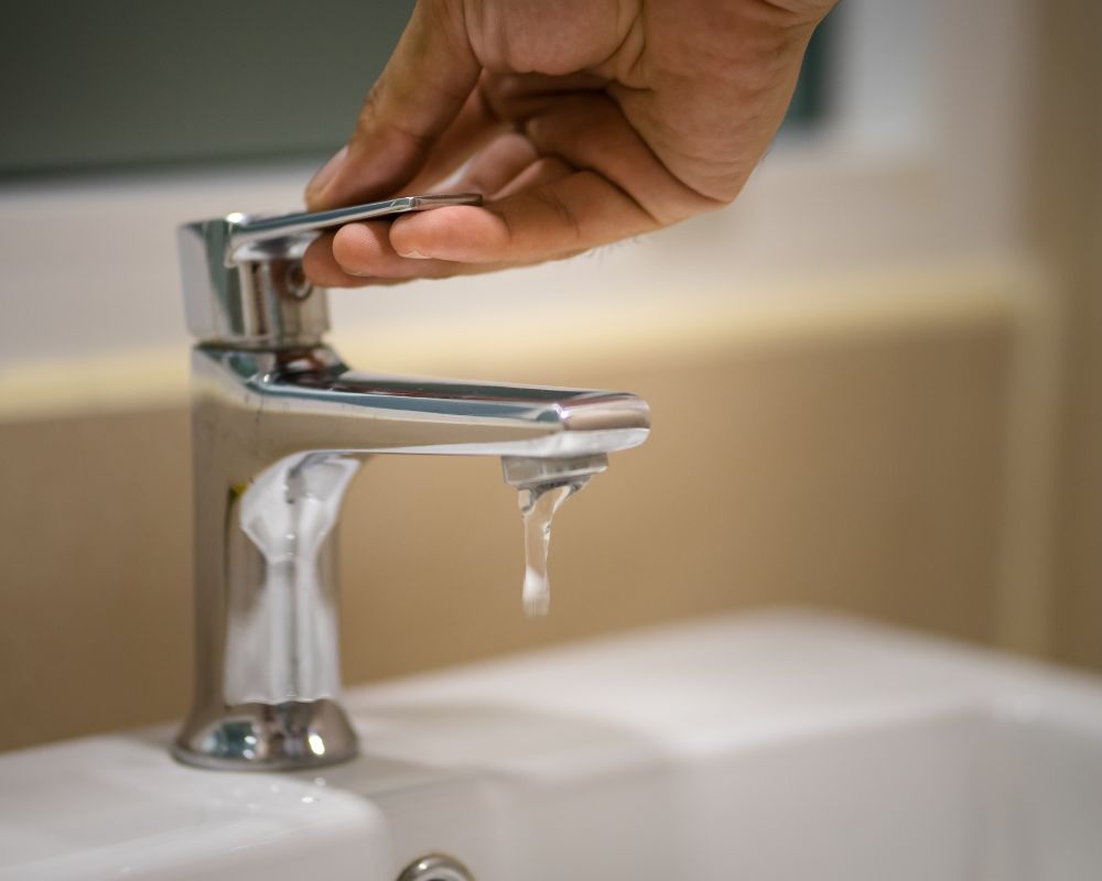 Hand turning off a faucet with a water drip